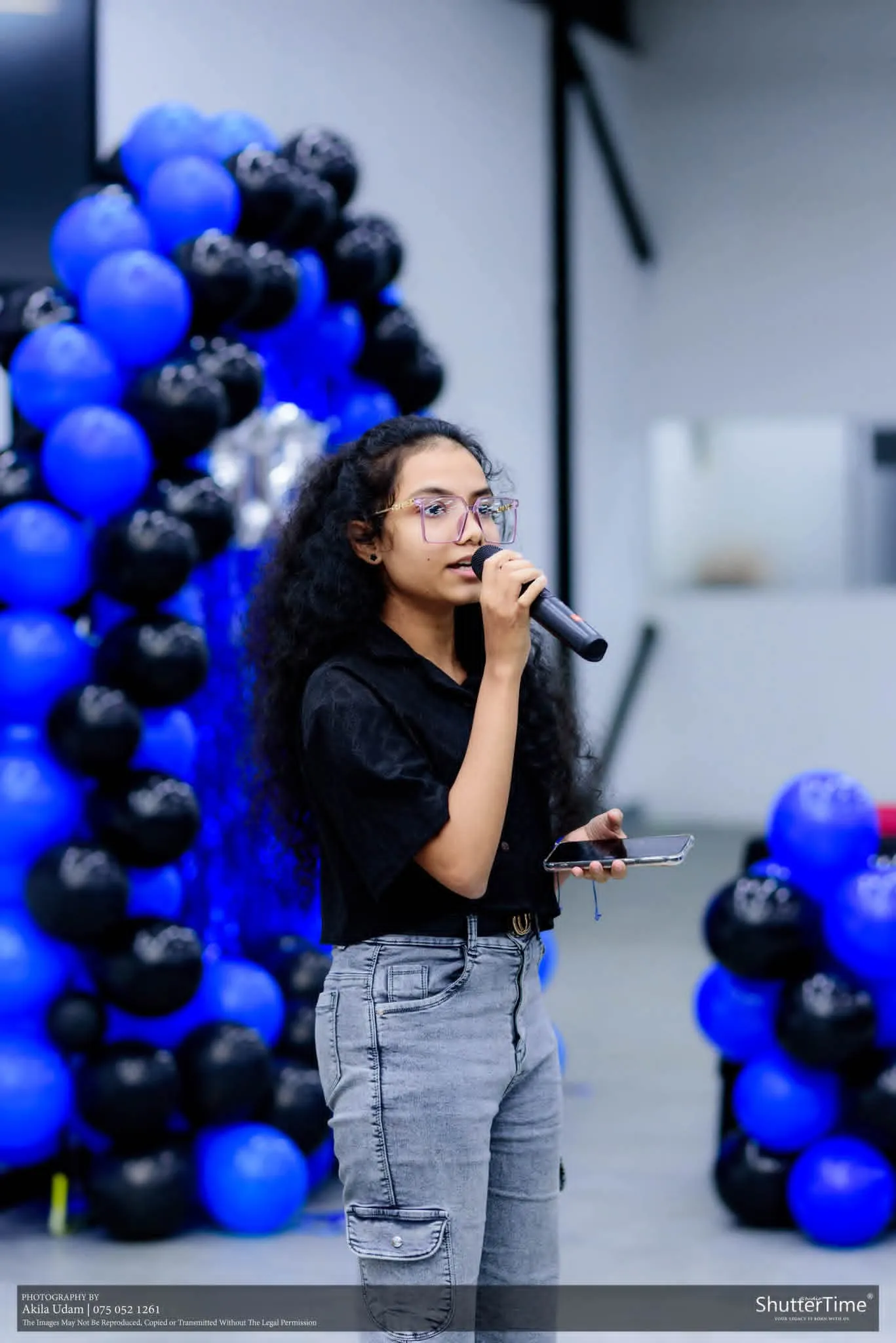 සිසුවියක් බැලූන් තොරණක් ඉදිරිපිට මයික්‍රොෆෝනයකින් ගී ගයමින්