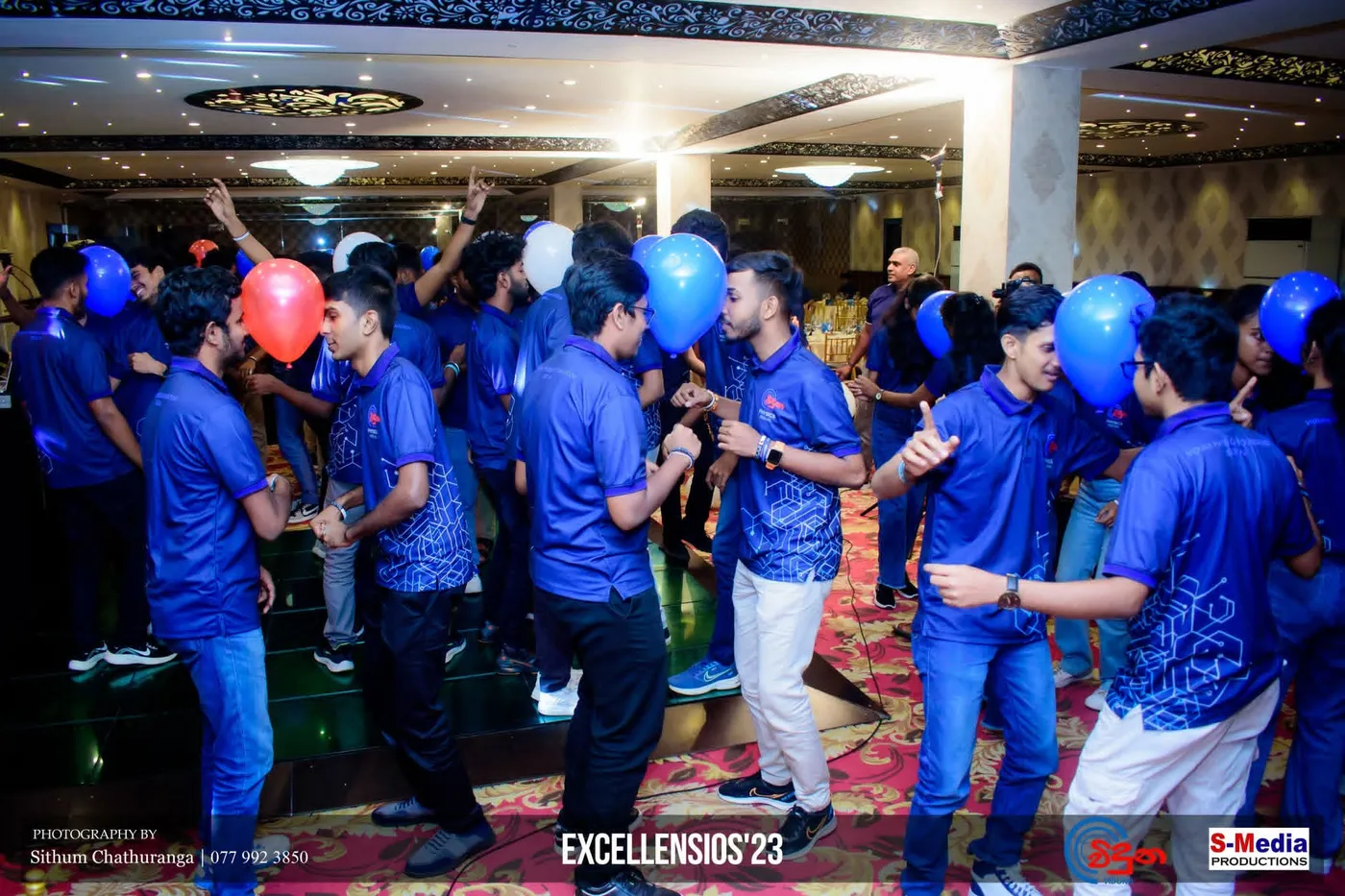 නිල් කමිස ඇඳි සිසුන් සමූහයක් උත්සව ශාලාවක නටමින්