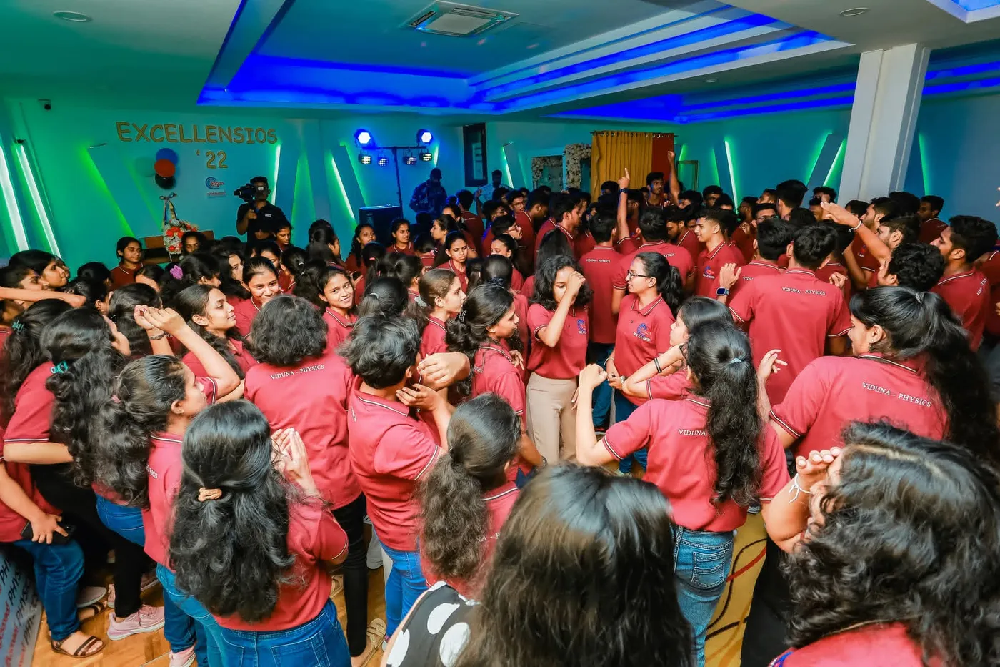 රතු කමිස ඇඳි සිසුන් සමූහයක්, EXCELLENSIOS'22 පසුබිම ඉදිරිපිට