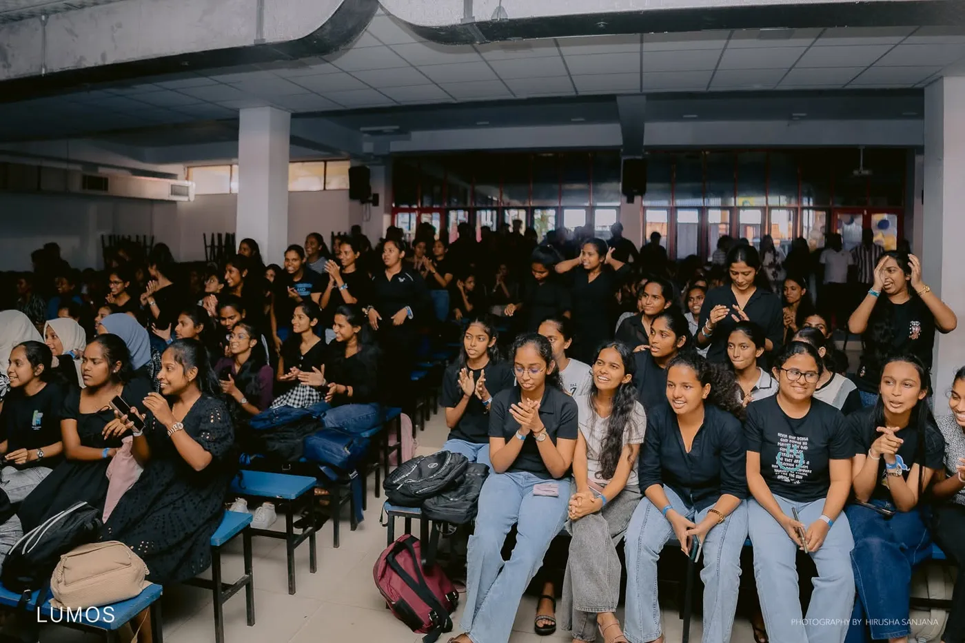 ශාලාවේ අසුන්ගත සිසුවියන් සහ සිසුන්, වේදිකා ප්‍රසංගය නරඹමින්
